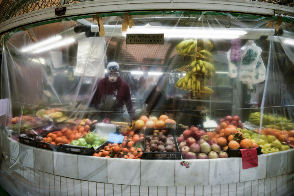 FILE - In this April 2, 2020, file photo, a worker wearing a face mask stands inside of a stall covered with a piece of plastic to prevent the spread of coronavirus, at a market in Pamplona, northern Spain. Grocery workers across the globe are working the front lines during lockdowns meant to keep the coronavirus from spreading. (AP Photo/Alvaro Barrientos, File)