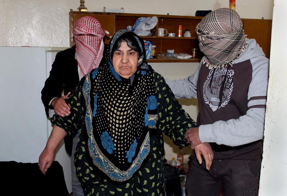 In this Feb. 11, 2014, masked anti-government gunmen help an elderly woman in Fallujah, Iraq. Islamic militants who took over the Iraqi city of Fallujah are now trying to show they can run it, providing social services, policing the streets and implementing Shariah rulings in a bid to win the support of its Sunni Muslim population. (AP Photo)
