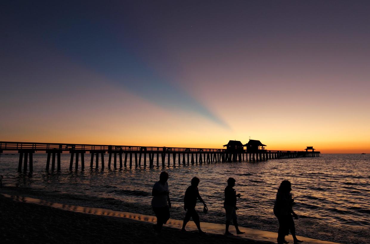 Beachgoers walk along the Gulf shore near the Naples Pier at sunset. Naples annually makes many national "best" lists. 