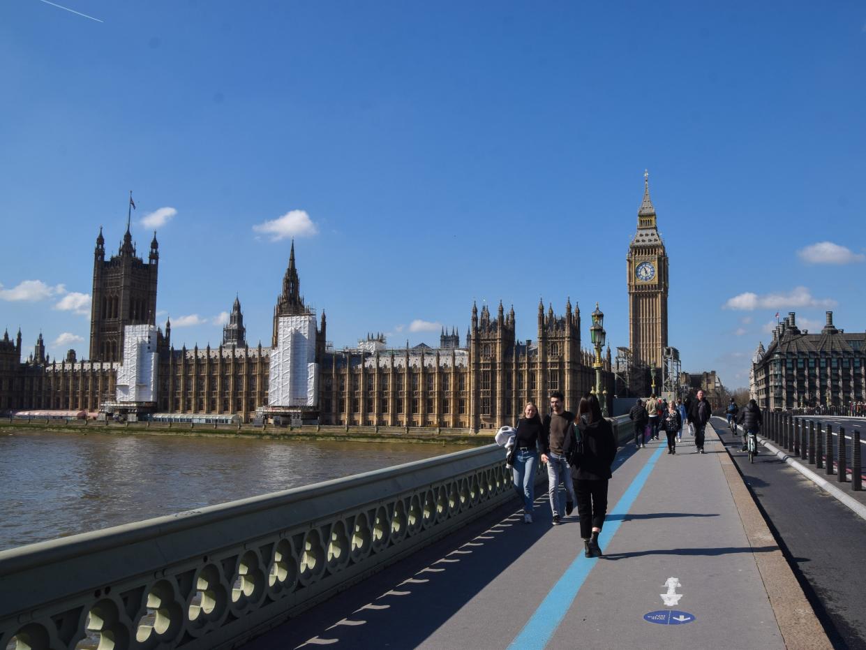 People walk across Westminster Bridge past the Houses of Parliament and Big Ben on a clear day.