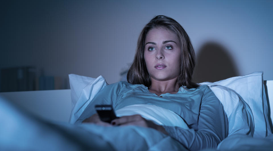Young woman relaxing in bed late at night and watching tv, she is holding a remote control