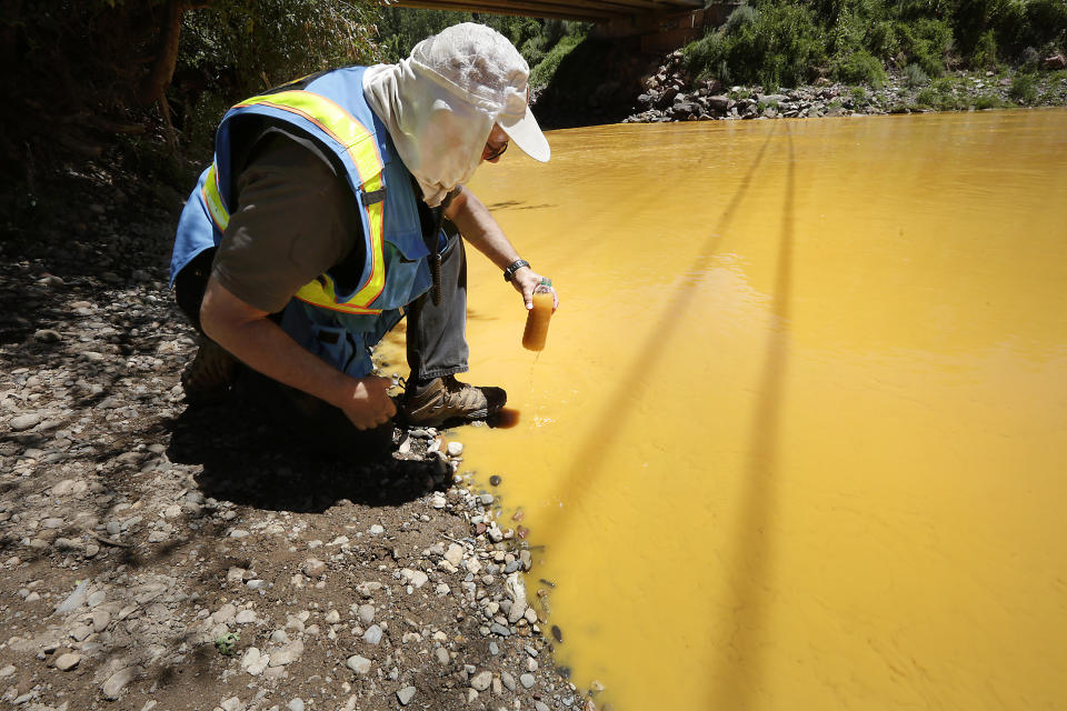 FILE - In this Aug. 6, 2015 file photo, Dan Bender, with the La Plata County Sheriff's Office, takes a water sample from the Animas River near Durango, Colo. after the accidental release of an estimated 3 million gallons of waste from the Gold King Mine. Federal officials fear that at least six of the sites examined by The Associated Press could have blowouts like the one at Gold King. (Jerry McBride/The Durango Herald via AP, File)