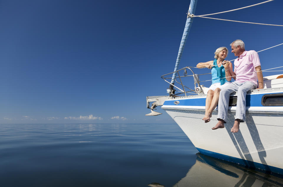 Happy senior couple sitting on the prow of a sailing boat on a calm blue sea