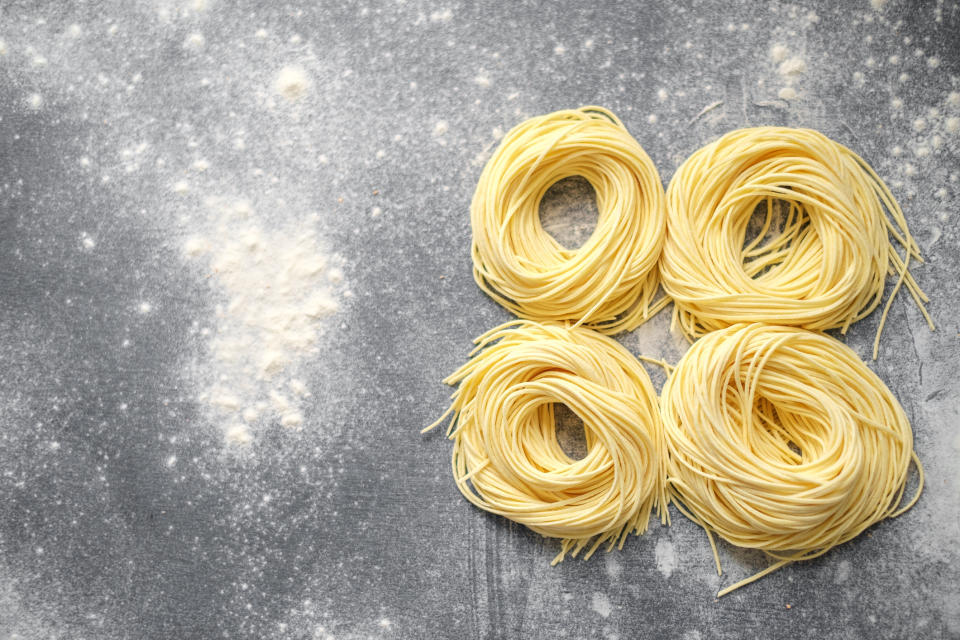 Four nests of uncooked spaghetti are arranged on a floured surface