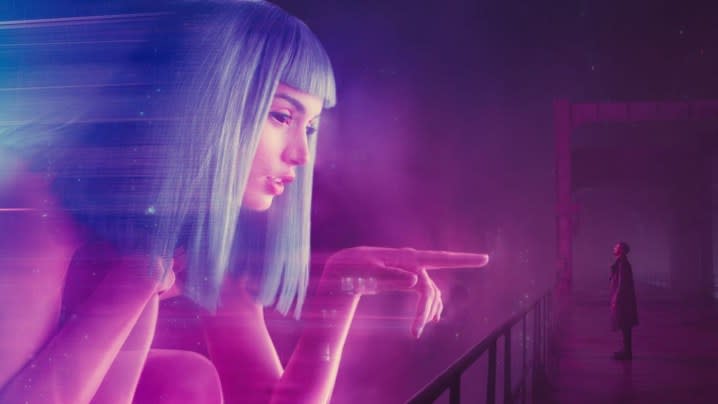 Officer K looking up at a neon-colored hologram in Blade Runner 2049.