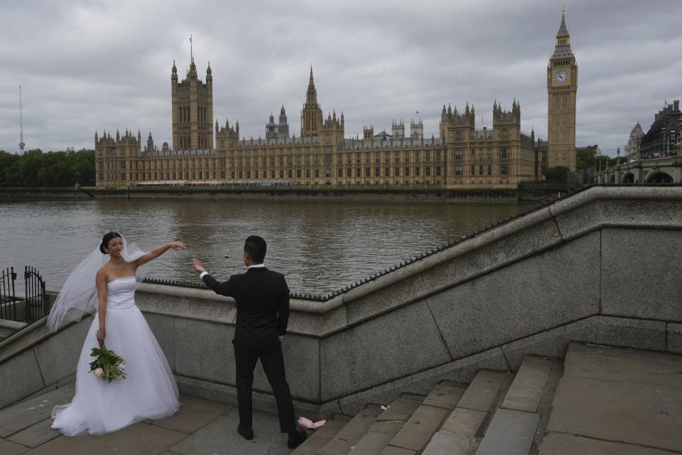 A couple take photograph outside the Houses of Parliament in London, Thursday, May 23, 2024. (AP Photo/Kin Cheung)