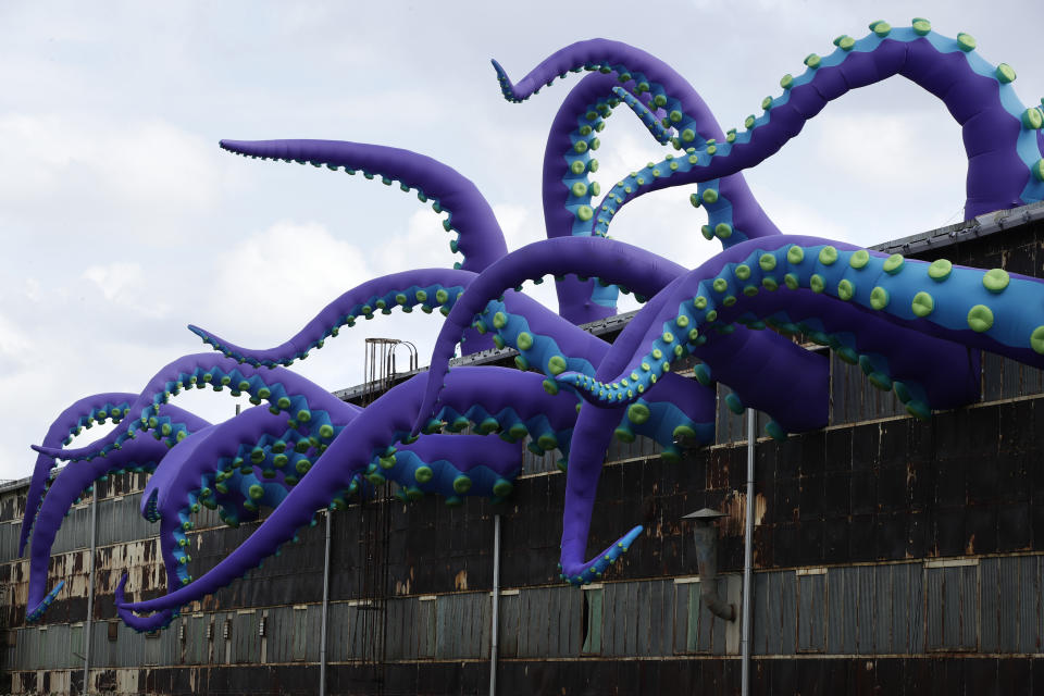 An inflatable sculpture entitled "Sea Monsters HERE" extends from a rusting warehouse called Building 61 at the Navy Yard in Philadelphia, Tuesday, Oct. 9, 2018. The installation was created by UK-based artists Filthy Luker and Pedro Estrellas. The former military base is free and open to the public. (AP Photo/Matt Rourke)