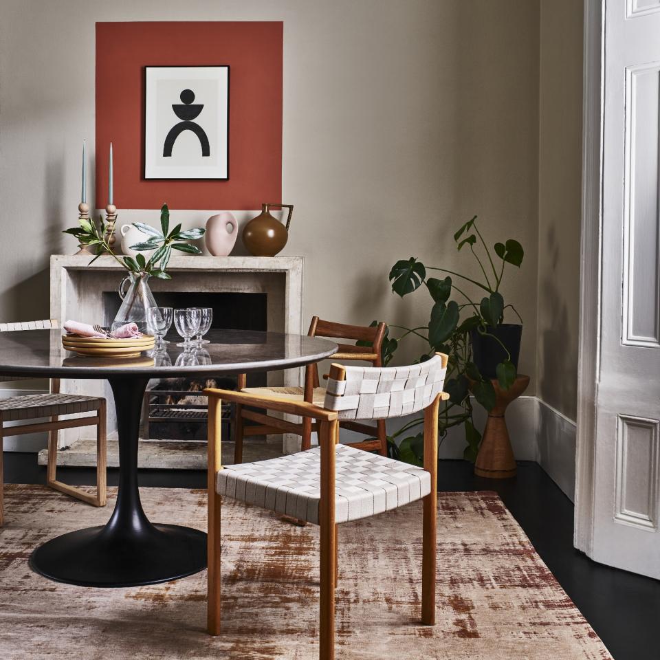 A dining room with a round dining table and woven chairs atop a patterned rug