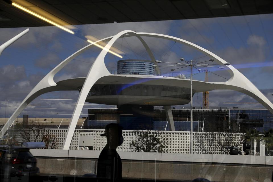 A masked traveler and the Theme Building are reflected in a window in a sparsely populated Terminal 4 at LAX