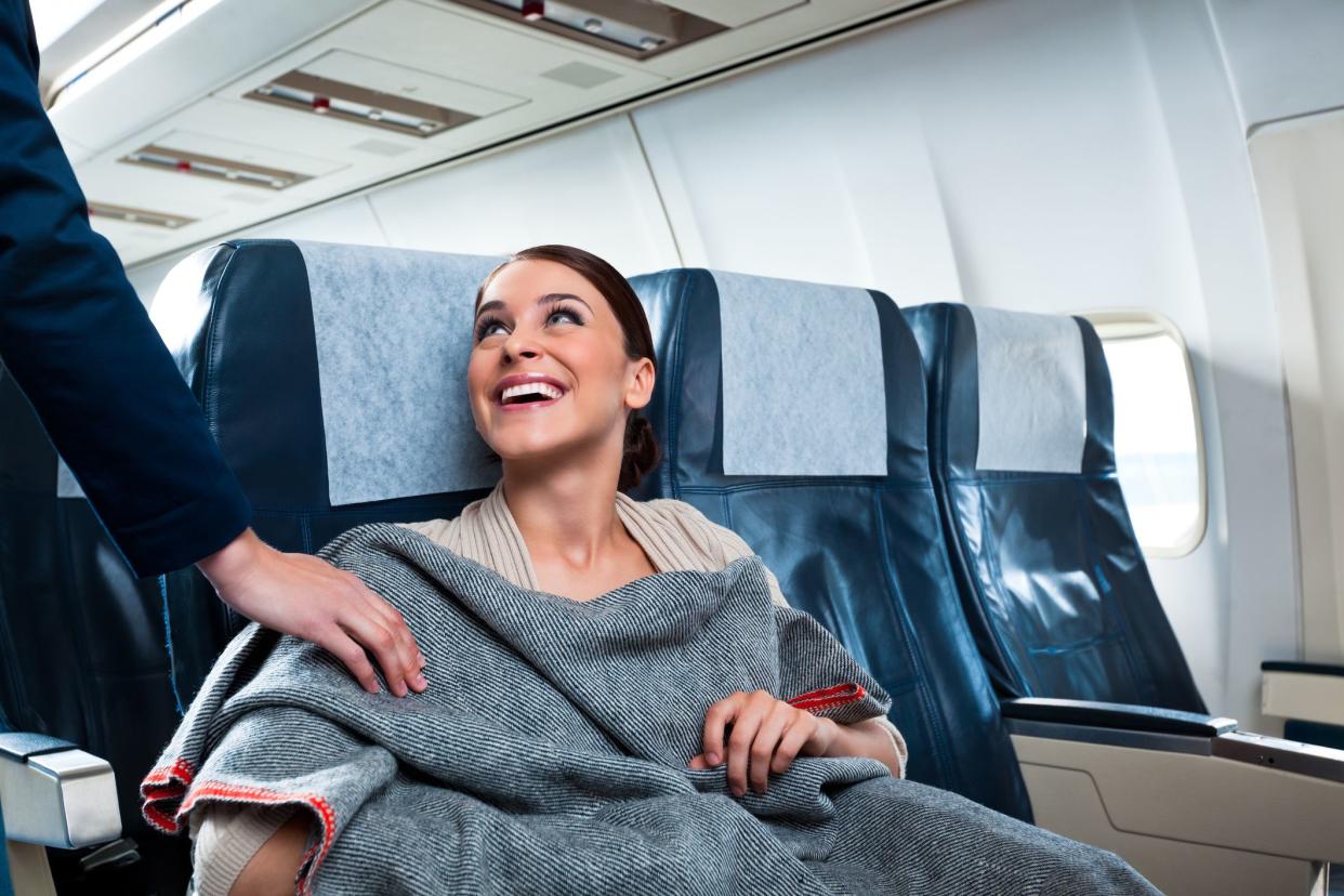 woman smiling gratefully receiving blanket from flight attendant
