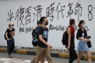 Protesters walk past a wall with spray-painted slogans during a demonstration in Hong Kong, Saturday, Aug. 3, 2019. Hong Kong protesters ignored police warnings and streamed past the designated endpoint for a rally Saturday in the latest of a series of demonstrations targeting the government of the semi-autonomous Chinese territory. (AP Photo/Vincent Thian)