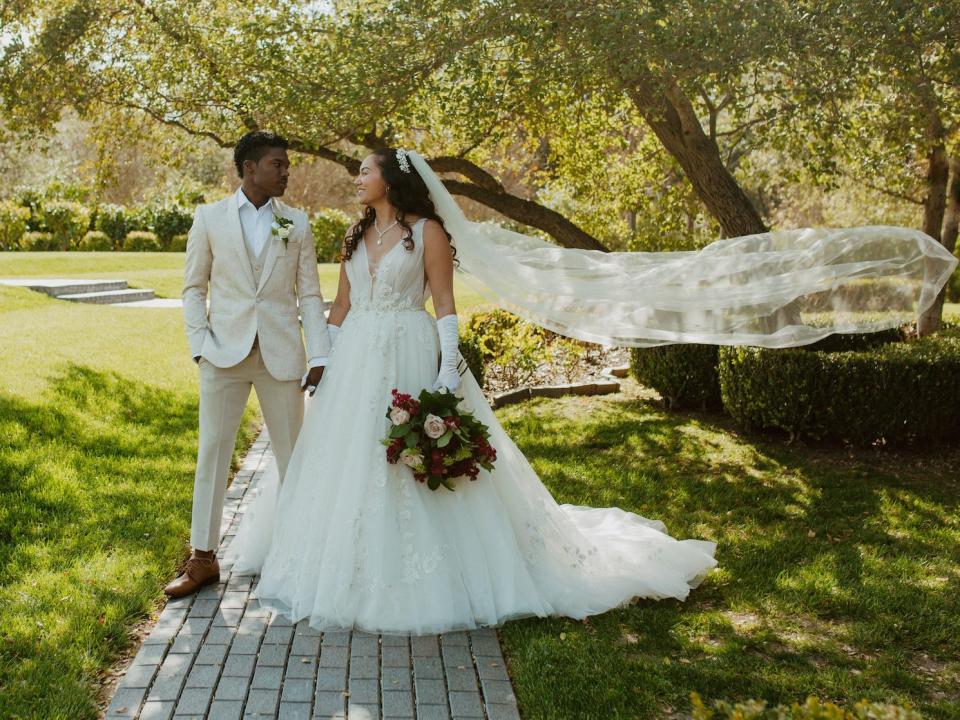 A bride and groom stand in a field looking at each other.