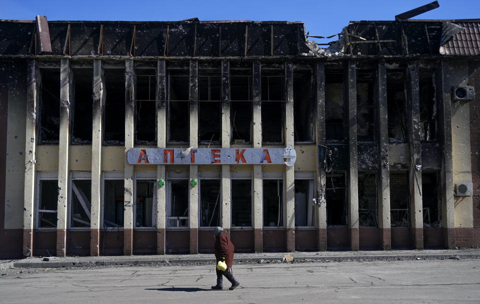 A woman walks past a heavily damaged building with a large sign that reads Pharmacy in Ukrainian.