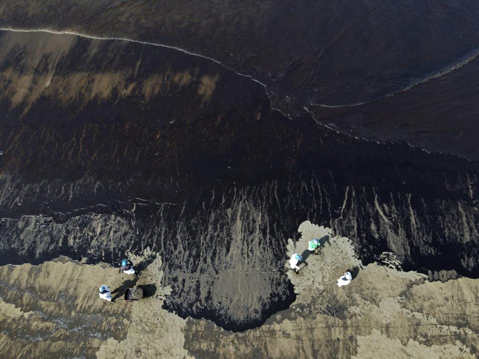 Workers clean oil from Cavero beach in Ventanilla, Callao, Peru, on Jan. 18, 2022. The Peruvian Civil Defense Institute said the eruption of an undersea volcano in Tonga created high waves that moved a ship loading oil into La Pampilla refinery, causing the oil to spill. (AP Photo/Martin Mejia)