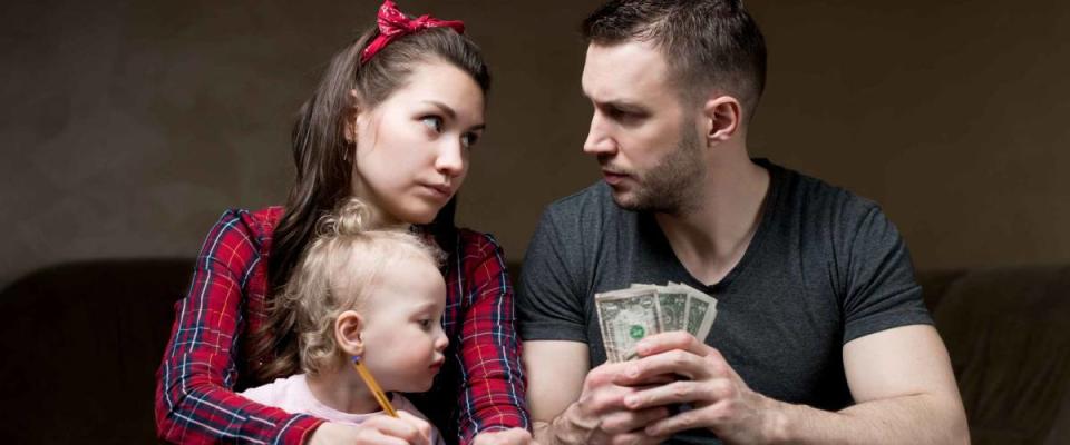 Counting family money. Husband and wife look at each other seriously, a little daughter sits on his wife s lap. Financial difficulties in a young family, crisis, lack of money