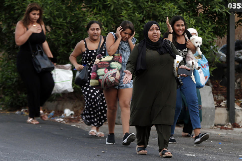 People cover their ears and carry their belongings as they flee their houses after heavy clashes in the coastal town of Khaldeh, south of Beirut, Lebanon, Sunday, Aug. 1, 2021. At least two people were killed on Sunday south of the Lebanese capital when gunmen opened fire at the funeral of a Hezbollah commander who was killed a day earlier, an official from the group said. (AP Photo/Bilal Hussein)