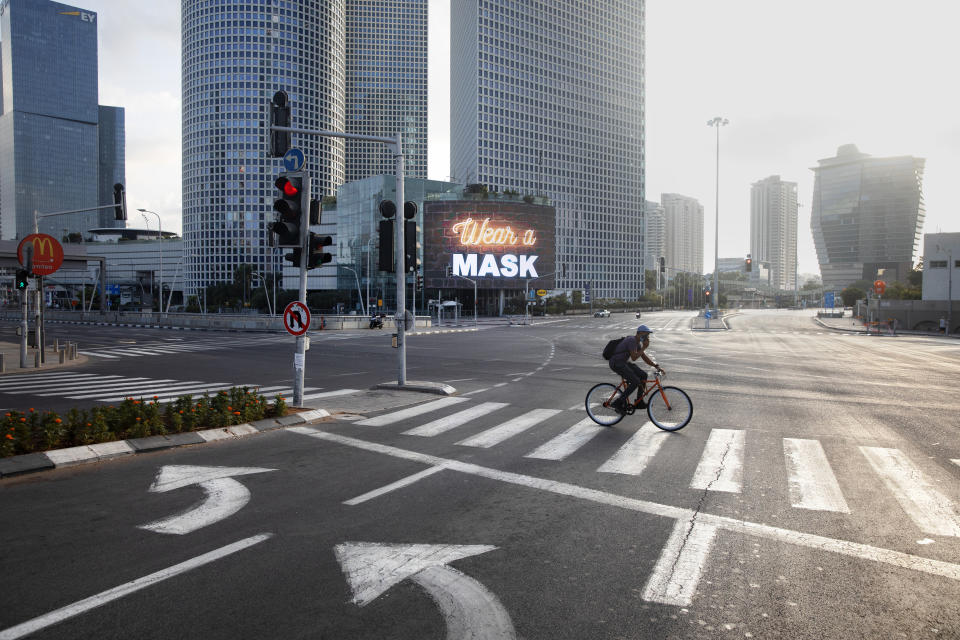 A man rides a bicycle next to a billboard calling people to wear masks, on empty road following new restrictions in the three-week nationwide lockdown, in Tel Aviv, Israel, Saturday, Sept. 26, 2020. (AP Photo/Oded Balilty)