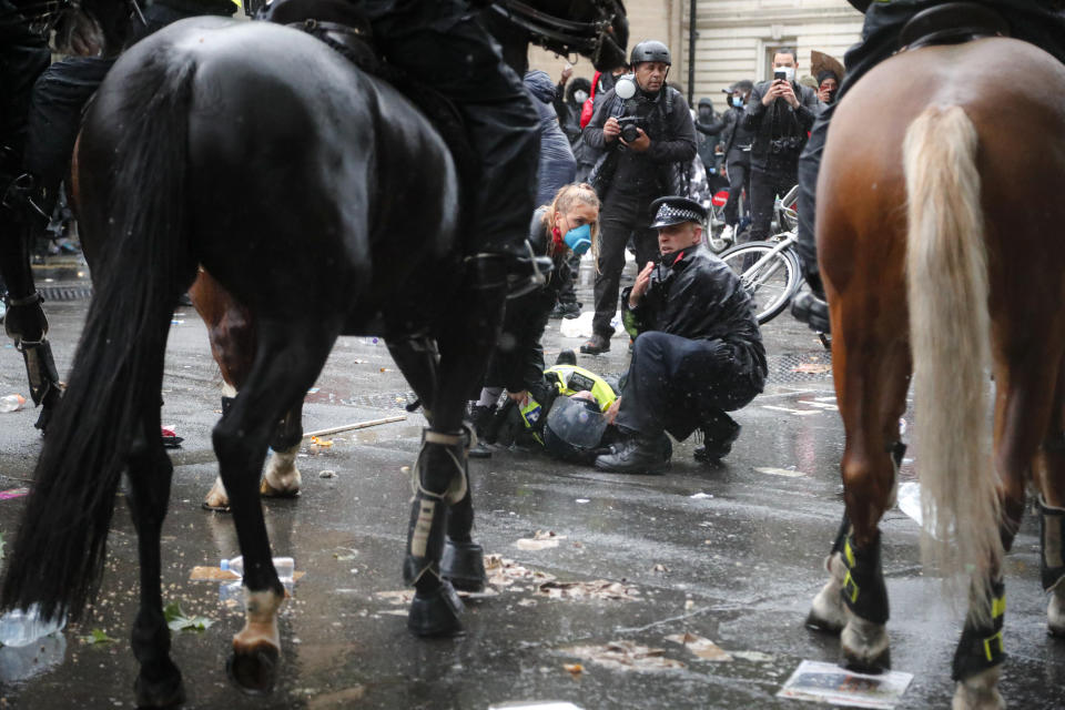 A colleague attends to a police officer who was injured when falling of a horse during scuffles with demonstrators at Downing Street during a Black Lives Matter march in London, Saturday, June 6, 2020, as people protest against the killing of George Floyd by police officers in Minneapolis, USA. Floyd, a black man, died after he was restrained by Minneapolis police while in custody on May 25 in Minnesota. (AP Photo/Frank Augstein)