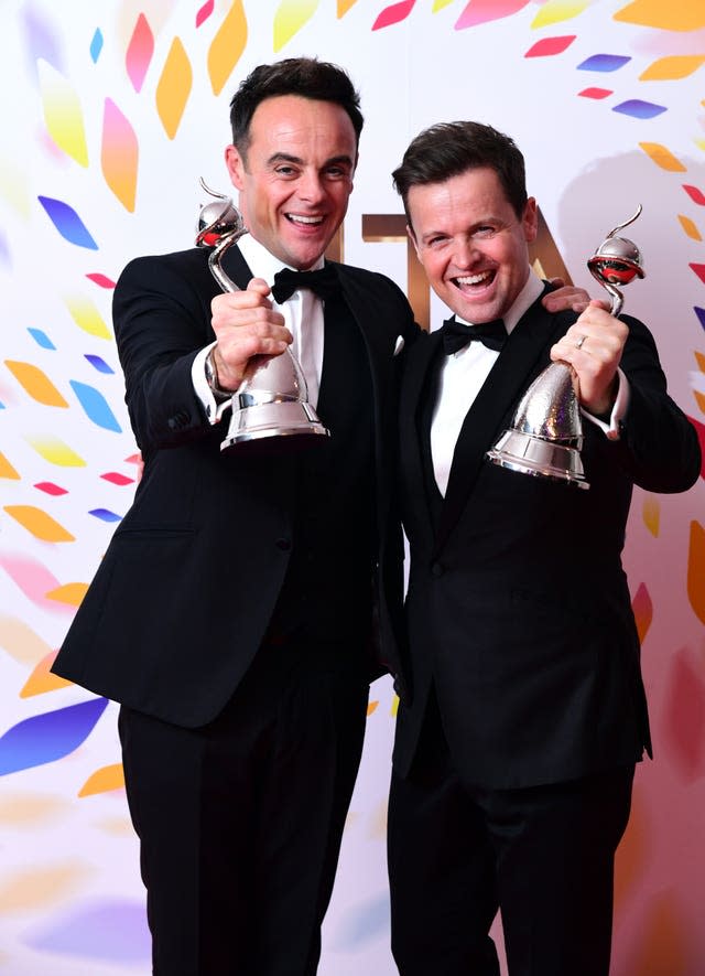 Two men in dinner suits hold their awards to the camera