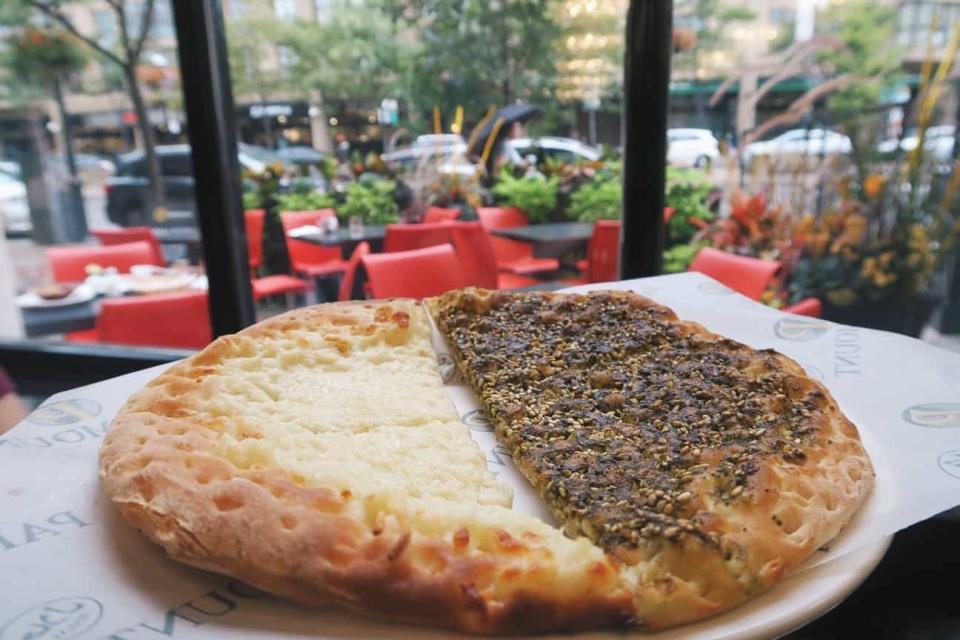 Half cheese, half za'atar manakish on a plate, viewed from indoors with a street-side cafe in the background