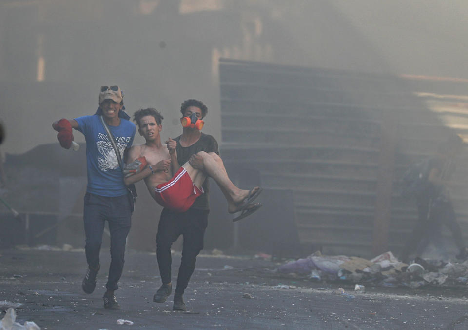 An injured protester is rushed to a hospital Iraqi riot police fire tear gas during clashes between Iraqi security forces and anti-government protesters in the al-Rasheed street in Baghdad, Iraq, Friday, Nov. 8, 2019. The demonstrators complain of widespread corruption, lack of job opportunities and poor basic services, including regular power cuts despite Iraq's vast oil reserves. They have snubbed limited economic reforms proposed by the government, calling for it to resign. (AP Photo/Khalid Mohammed)