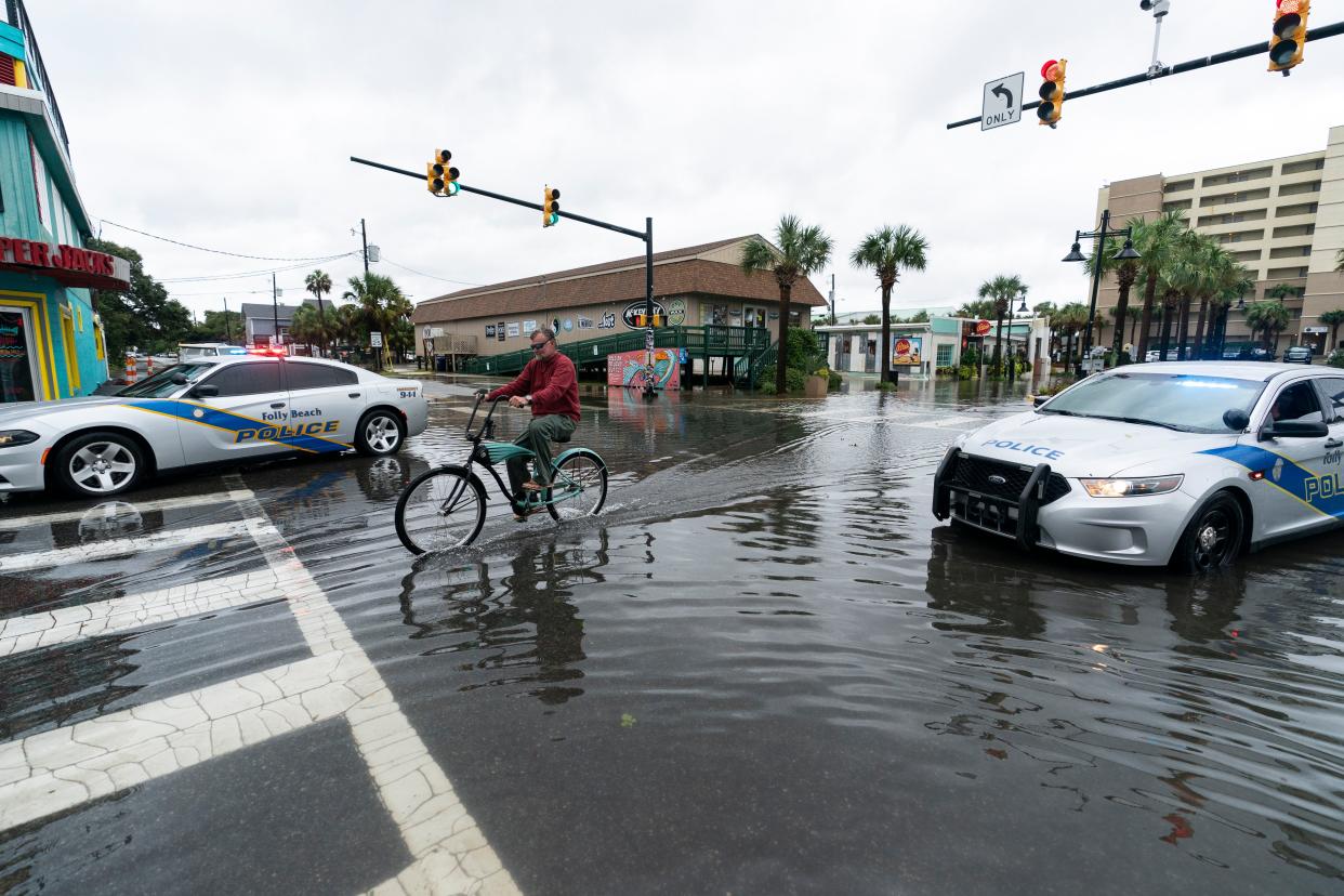 A bicyclist rides through the standing water as law enforcement blocks the intersection to traffic, during the effects from Hurricane Ian, Friday, Sept. 30, 2022, in Folly Island, S.C. 