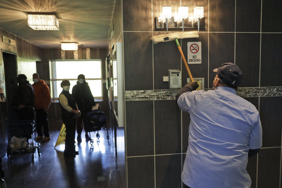 Residents watch as members of the janitorial staff wipe down the lobby of a building in Co-op City in the Bronx borough of New York, Wednesday, May 13, 2020. Regular cleanings occur throughout the common areas of the buildings while the heavy disinfecting occurs in response to specific incidents, in this case reports of two coronavirus cases on the same floor. (AP Photo/Seth Wenig)