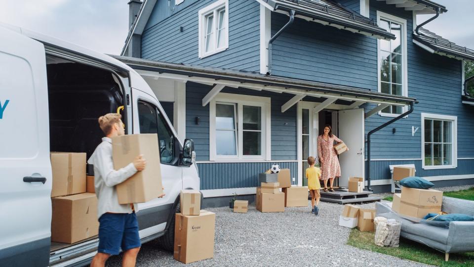 young son helping parents to unload a cargo van with furniture and accessories for their new home in successful residential area kid bringing a plant to his mother family moving to their new home