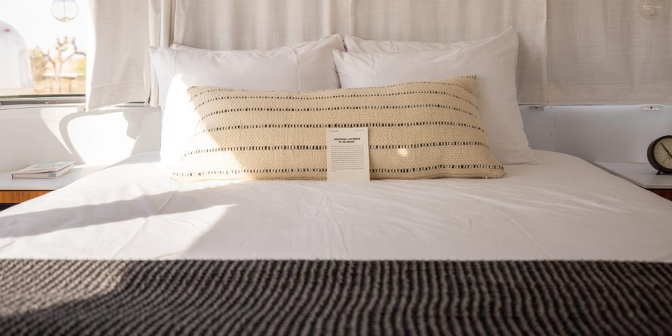 A bedroom inside Autocamp Joshua Tree's Airsteram trailer with white accents, a bed with pillows, curtains over windows.