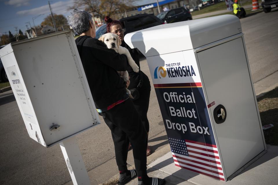 A woman carries her puppy as she drops off her ballot at Kenosha's municipal offices for early voting in Kenosha, Wis., Friday, Oct. 30, 2020. Trump has made protest violence in Kenosha and other American cities, a key part of his re-election campaign, linking violence to Democrats and saying it would spread dramatically if Democratic nominee and former Vice President Joe Biden was to defeat him on Election Day. (AP Photo/Wong Maye-E)