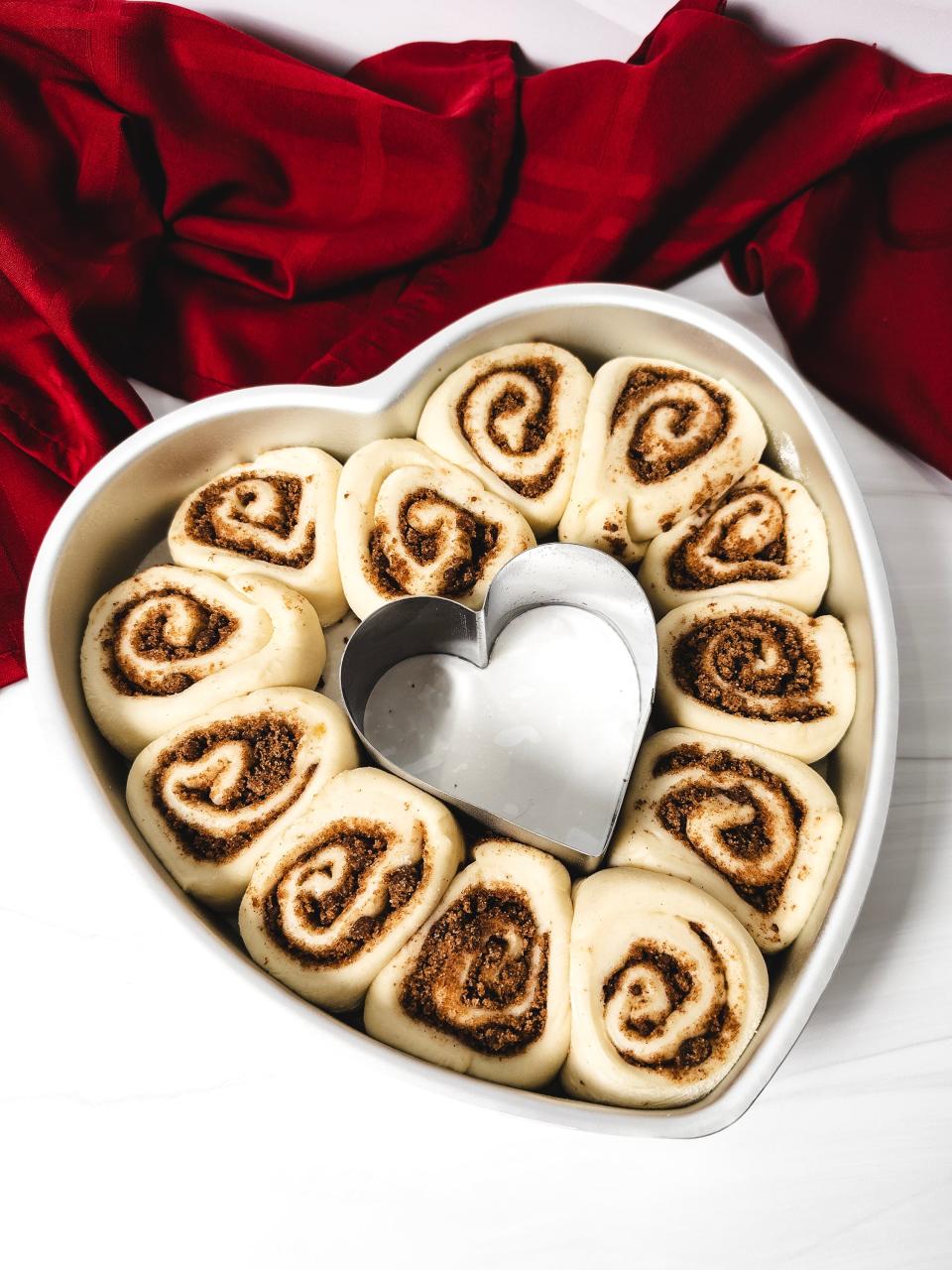 Cut the cinnamon-filled dough into cinnamon rolls and place in a heart-shaped pan to let the yeast work its magic.