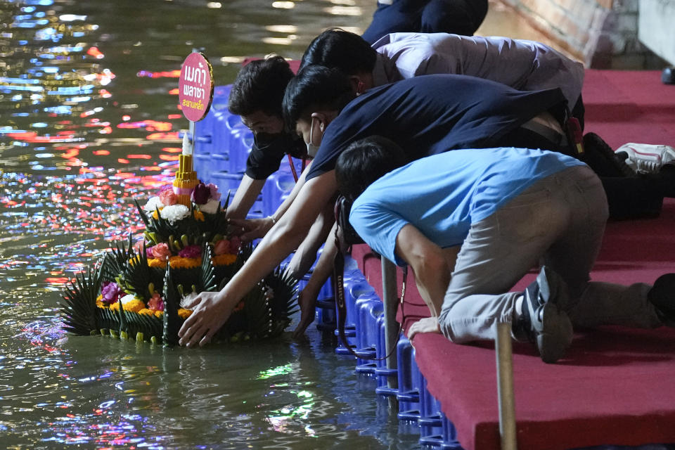 Thais place a krathong, a small boat made of banana tree and decorated with banana leaves and flowers, into a Ong Ang canal during Loy Krathong festival in Bangkok, Thailand, Friday, Nov. 19, 2021. Thais believe that the candle-lit boats launched during the charming and popular Loy Krathong festival can carry the year's misfortunes away with them, but workers must clean up the waterways afterward to keep them from getting clogged and polluted. (AP Photo/Sakchai Lalit)