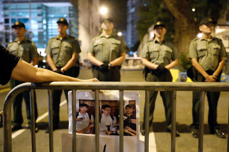 A protester holds a photo of jailed Hong Kong student leaders Joshua Wong, Nathan Law and Alex Chow (L-R), while officers from the Correctional Services Department standing guard outside a prison in Hong Kong, China August 18, 2017. REUTERS/Tyrone Siu