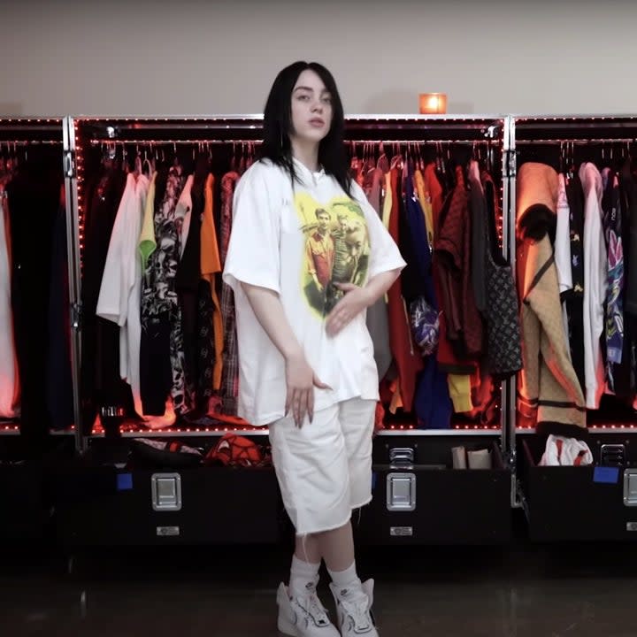 Billie stands in front of several road cases filled with clothing that is hung up