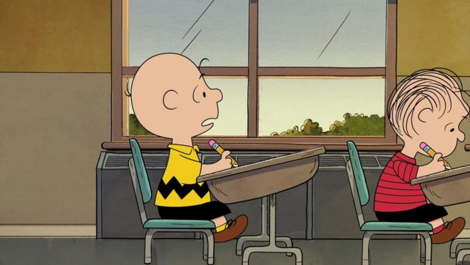 a photo of Peanuts character Charlie Brown sitting at a desk with a friend in front of him.