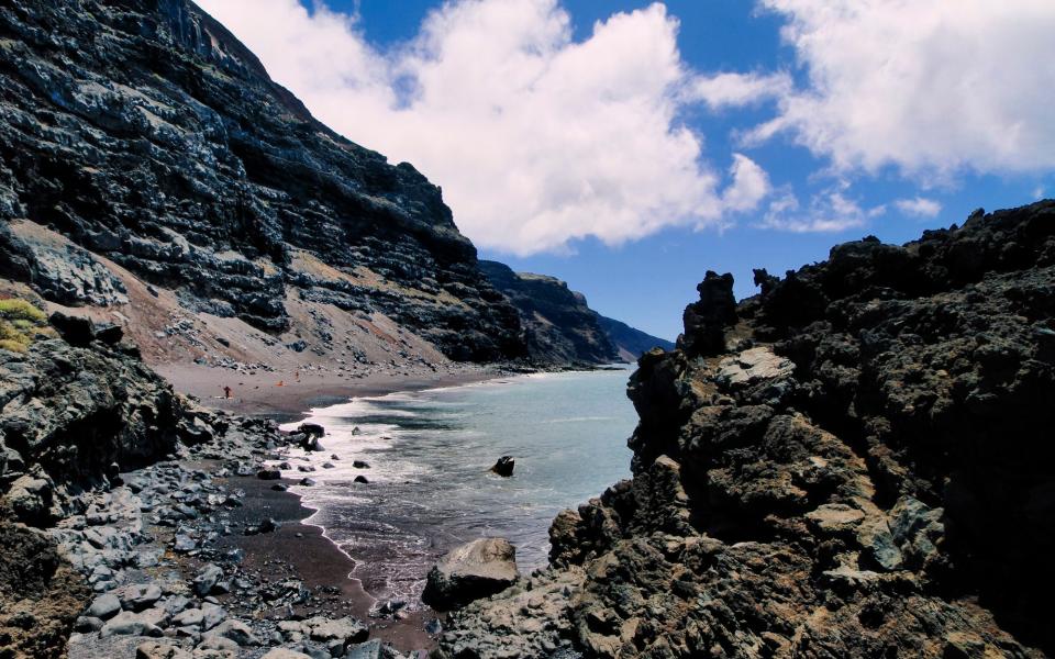 Black-sand beach surrounded by rugged cliffs - iStockphoto 