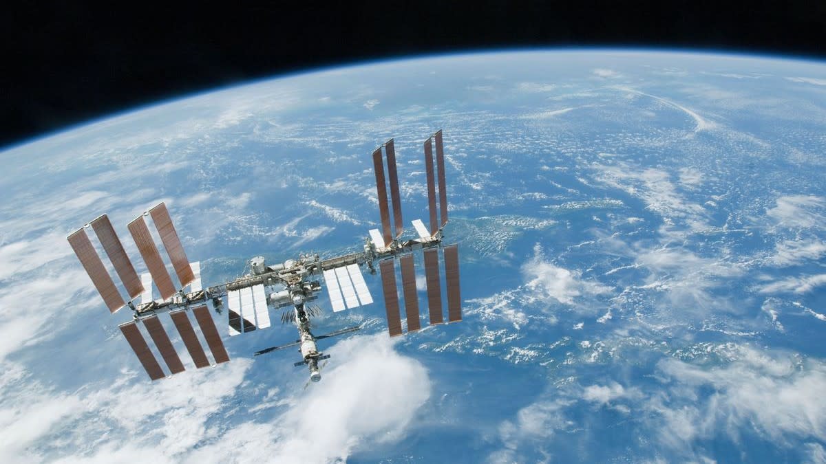  A T-shaped space station with multiple solar arrays floats above earth. 