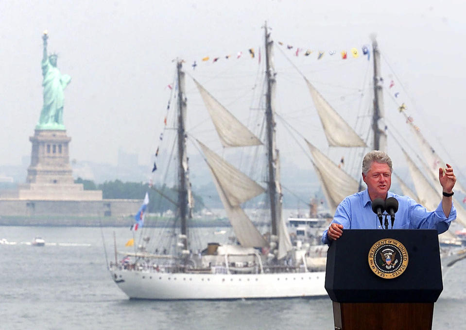 FILE - President Bill Clinton speaks on the USS John F. Kennedy as a tall ship passes between him and the Statue of Liberty in New York Harbor during Independence Day celebrations in New York, July 4, 2000. (AP Photo/Ed Betz, File)