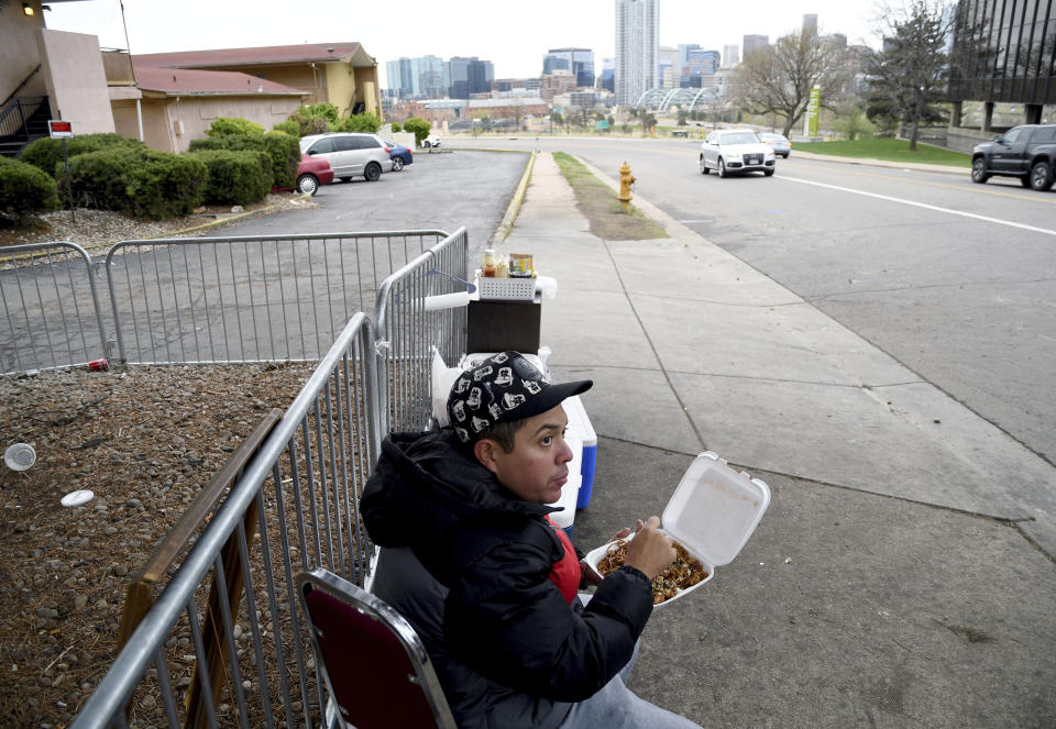 Lincoln Montero eats outside a motel designated for migrants after helping his aunt Yesenia sell home-cooked Venezuelan-style food to fellow Venezuelan migrants sheltering here in Denver, Colorado, Thursday, April 18, 2024. Montero said he traveled to Denver the week before, to unite with his aunt who has been here four months. (AP Photo/Thomas Peipert)