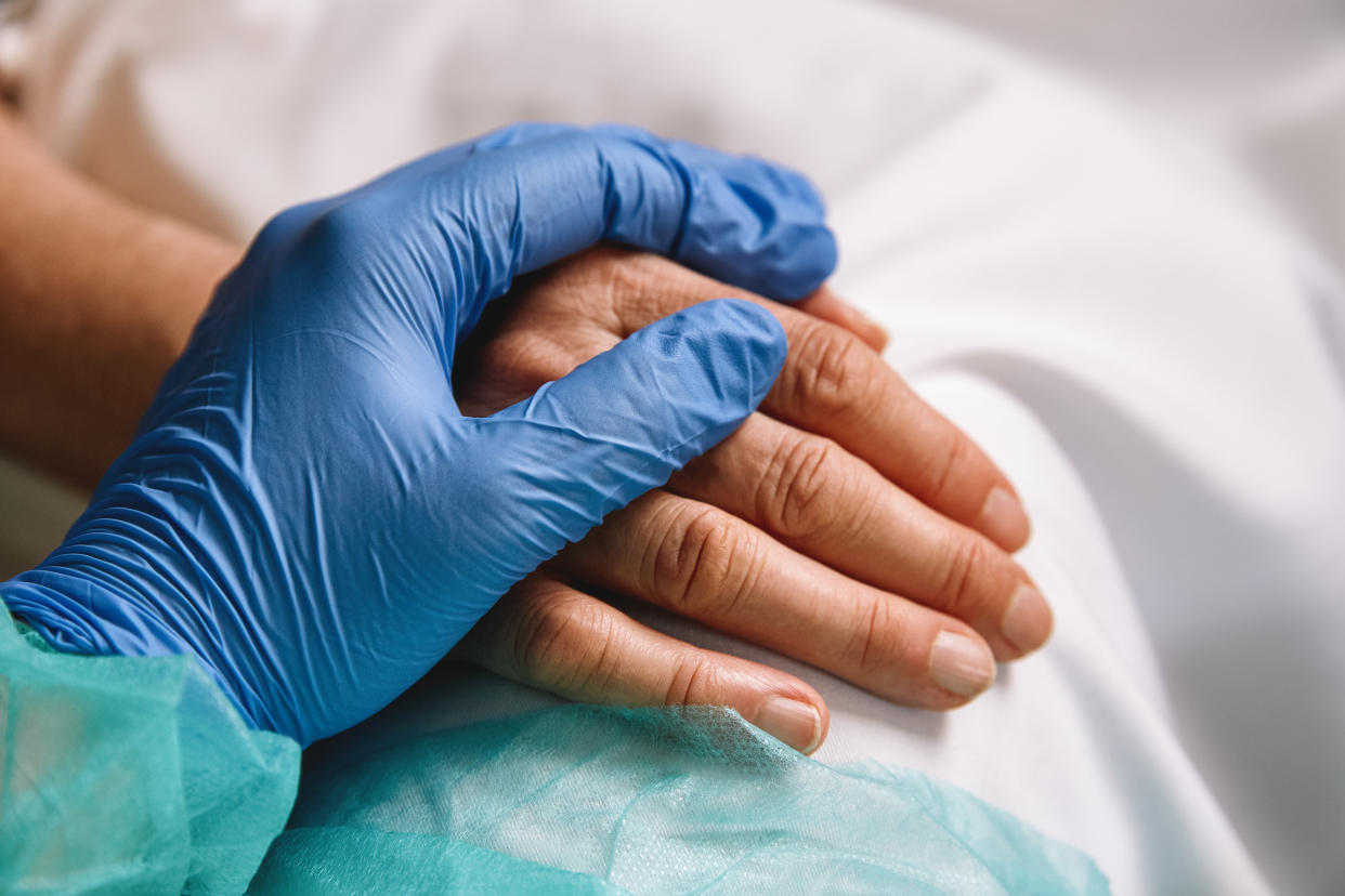 Close up of a doctor hand with blue glove giving support and love to a patient at hospital. Coronavirus pandemic concept.