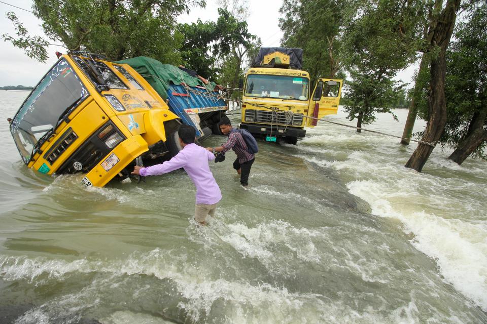 People wade past stranded trucks on a flooded street in Sunamganj, Bangladesh, in June. 