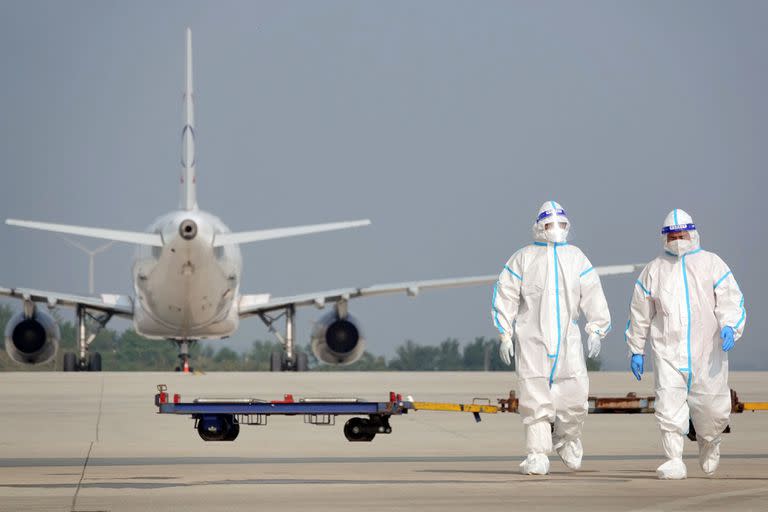 Esta foto de archivo tomada el 18 de septiembre de 2022 muestra al personal de tierra de aviación con equipo de protección personal (EPP) trabajando en un avión que llegó desde el extranjero en el aeropuerto de Yantai, en la provincia oriental china de Shandong.