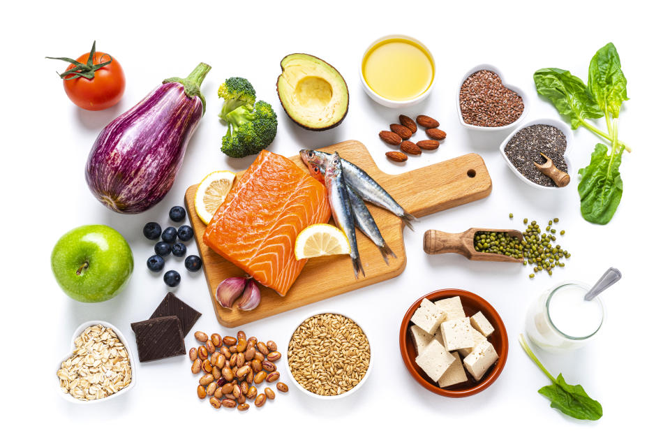 Healthy eating: group of fresh multicolored foods to help lower cholesterol levels shot from above on white background. The composition includes oily fish like salmon and sardines. Beans like Pinto beans and brown lentils. Vegetables like garlic, avocado, broccoli, eggplant and tomatoes. Fruits like apple, grape, orange and berries. Nuts like almonds and walnuts. Soy products like tofu and soy milk. Cereals and seeds like chia seeds, flax seeds, oatmeal and barley. Olive oil and yogurt with added sterols and stanols. High resolution 42Mp studio digital capture taken with SONY A7rII and Zeiss Batis 40mm F2.0 CF lens