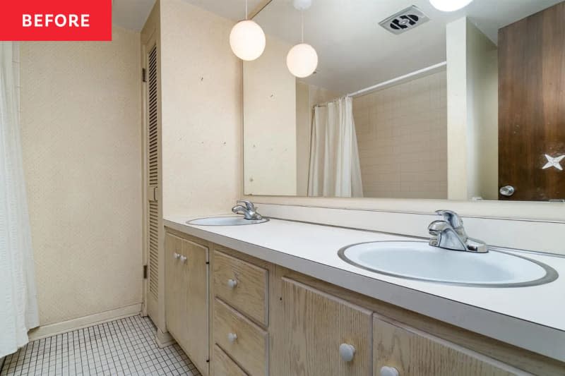 Bathroom before renovation: off white walls, white shower curtain with black stripes, 2 round bath mats, white small rectangular floor tiles, wood cabinets with black pulls, double sink with hanging globe pendant lights