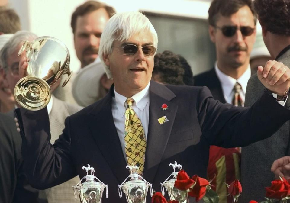 FILE - Real Quiet trainer Bob Baffert strikes a quarterback pose with the Kentucky Derby trophy after Real Quiet with jockey Kent Desormeaux up won the 124th running of the Kentucky Derby at Churchill Downs, in Louisville, Ky., May 2, 1998. Baffert will miss the race for the third consecutive year. He served a two-year suspension by Churchill Downs Inc. after his 2021 winner Medina Spirit was disqualified for a failed drug test. But the track’s corporate ownership meted out an additional year of punishment. (AP Photo/Ed Reinke, File)