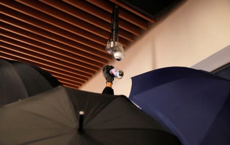 An anti-government protester is covered by umbrellas while spraying a CCTV camera during a demonstration at New Town Plaza shopping mall in Hong Kong