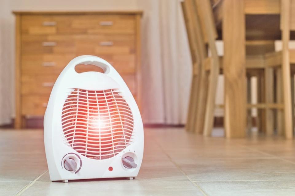 A white space heater in use on a kitchen floor with a wood kitchen table in the background.