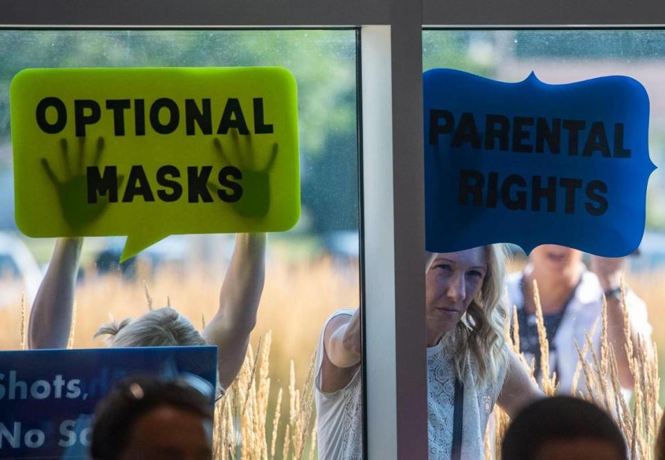 People stand with signs outside the Shawnee Mission School District board meeting Monday, listening on their phones as parents speak about their preferences for students wearing masks in the 2021-22 school year.