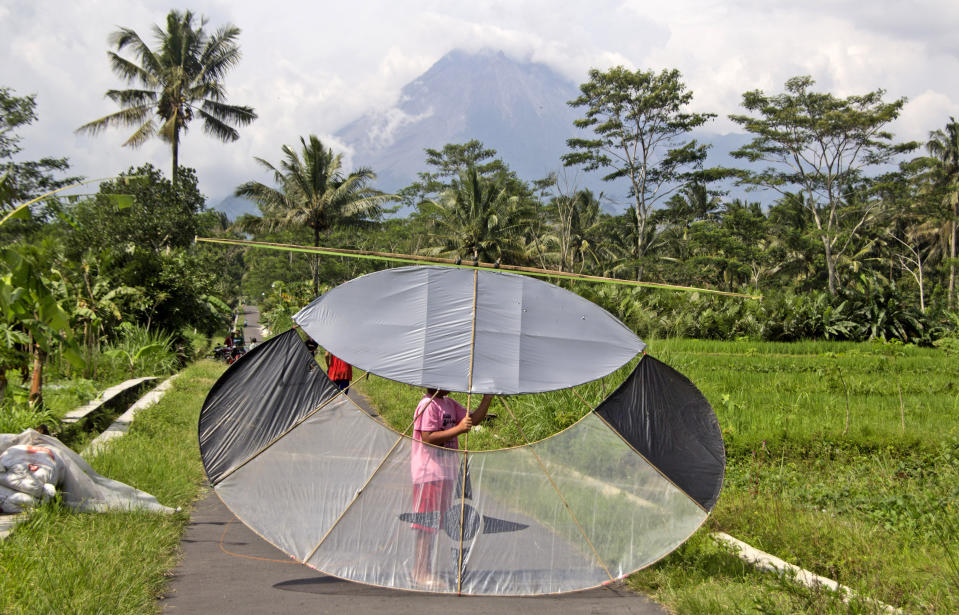 An Indonesian boy carries a kite as Mount Merapi is seen in the background in Sleman, Indonesia, Thursday, Nov. 5, 2020. Indonesian authorities raised the danger level for the volatile Mount Merapi volcano on the densely populated island of Java on Thursday and ordered a halt to tourism and mining activities. (AP Photo/Slamet Riyadi)