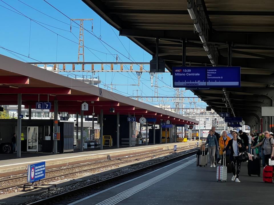 people walking down a train station platform geneva with bags